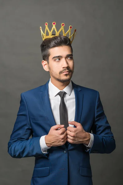 灰色の背景に彼の頭には王冠と紺のスーツの若い魅力的な男 — ストック写真