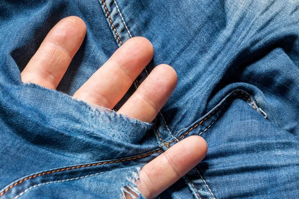 Human fingers sticks out from a hole in jeans