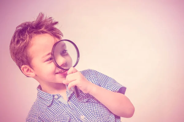 Cute boy with a magnifying glass near the face on a pink background. Toned