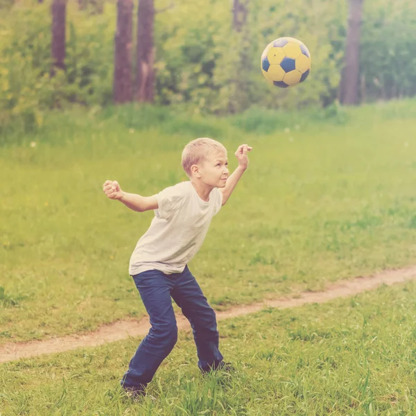 Blond boy playing with a ball in the park. Toned