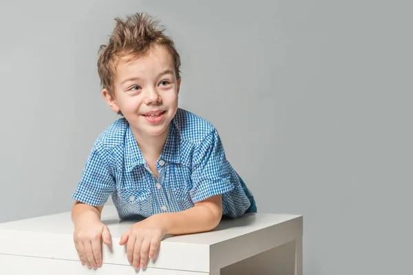 Cute boy in a blue shirt at the table on a gray background. Isolated