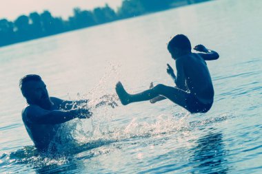 Suya atlamak. Erkek ve çocuk eğleniyor ve suya su sıçratıyorlar. Yaz tatili kavramı