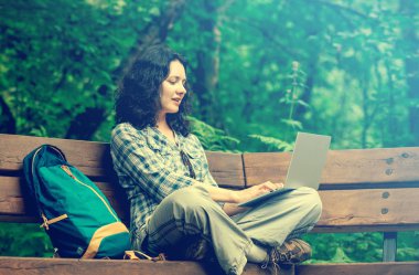 Parkta dizüstü bilgisayar kullanan seyahat eden kadın