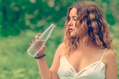 Güzel genç kadın doğa arka plan üzerinde bir cam şişe taze berrak su içme