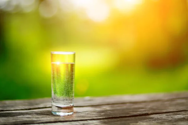 The glass of cool fresh water on a wooden table outdoors