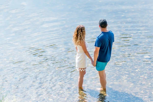 Aşık mutlu çift suda el ele tutuşarak duruyor. Sahilde genç adam ve kadın