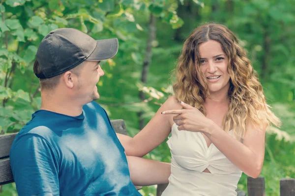 Young couple arguing on a bench in the summer park. Girl pointing finger at boyfriend.