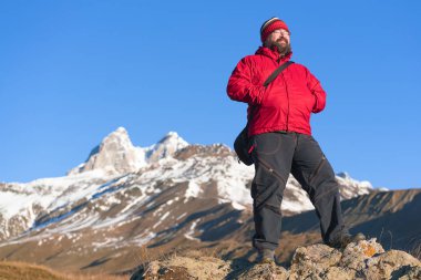Bir dağın tepesinde kırmızı ceketli sakallı adam.
