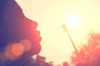 Gün batımında karahindiba üfleyen kız. Close.