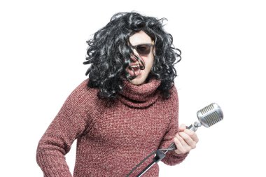 Peruk ve güneş gözlüğü takan bir adam mikrofon tutuyor..