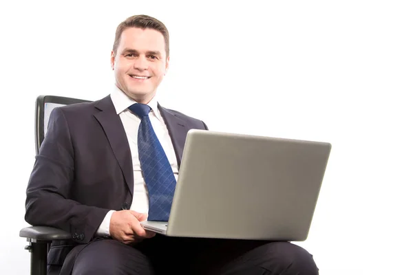 A smiling businessman holds a laptop while sitting in a chair. C — Stock Photo, Image