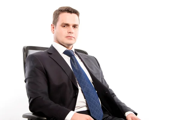 A serious man in a suit sits in a chair on a white background in — Stock Photo, Image