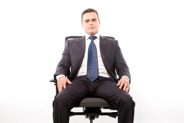 A serious man in a suit sits in a chair on a white background in — Stock Photo, Image