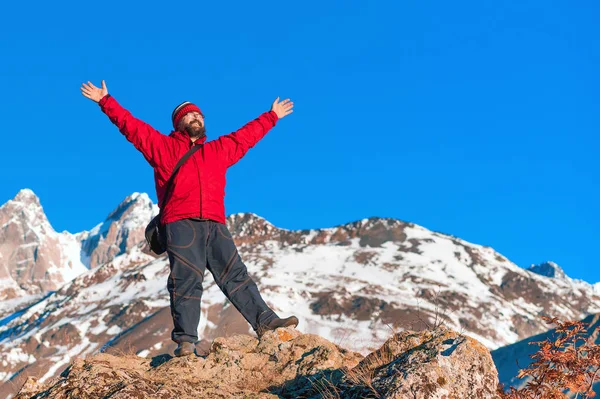 Muž v červeném kabátku s rukama nahoře v horách. — Stock fotografie