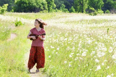 Çayır yolunda ukulele çalan şarkı söyleyen kız.