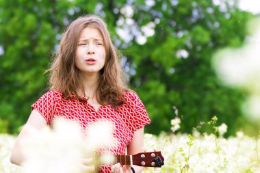 Üzgün kız şarkı ve çiçekler ve ağaçlar arasında ukulele oynuyor
