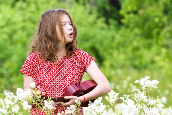 Співаюча дівчина з укулеле на лузі серед квітів — стокове фото