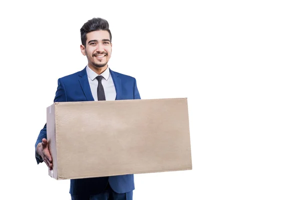 Atractivo hombre sonriente en un traje azul sosteniendo una caja de cartón en — Foto de Stock