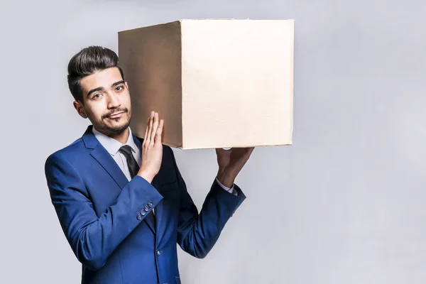 Ung man i en kostym håller en låda på axeln på en vit att — Stockfoto