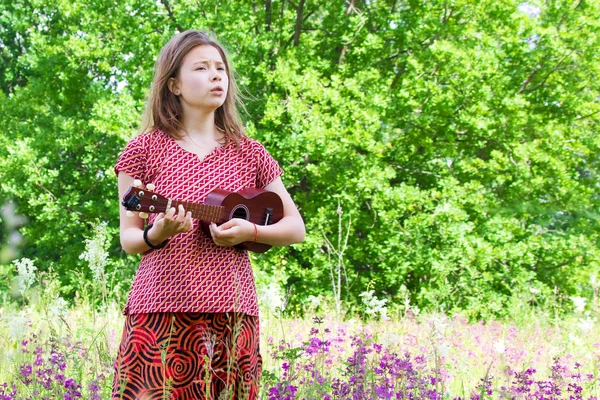 Sad girl sings and plays the ukulele on a green meadow. — Stock Photo, Image