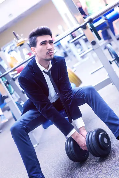 Businessman in suit lifts heavy dumbbell in the gym.