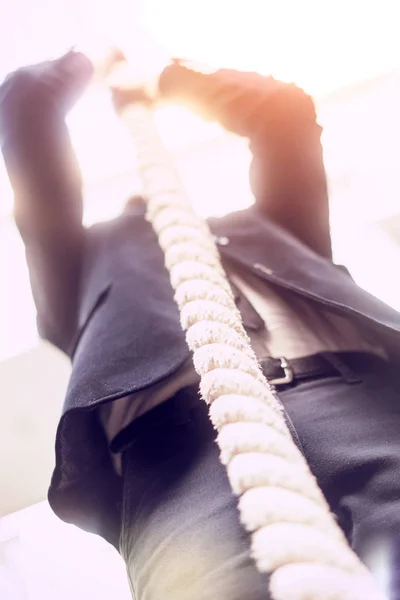 Giovane in camicia bianca e tuta sale la corda in palestra — Foto Stock