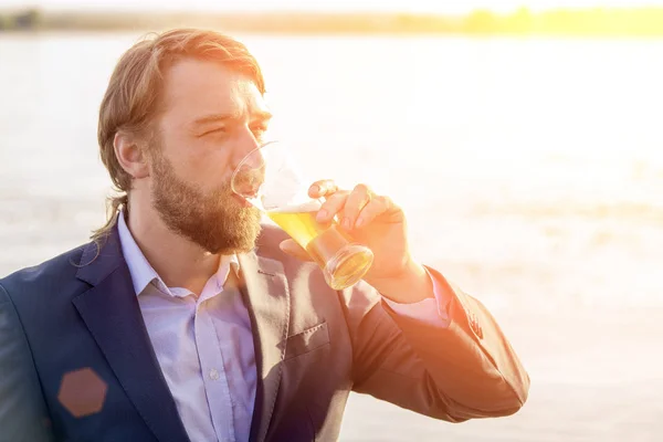 Vousatý muž ve svěrací kazajce s pivem v ruce na pozadí — Stock fotografie