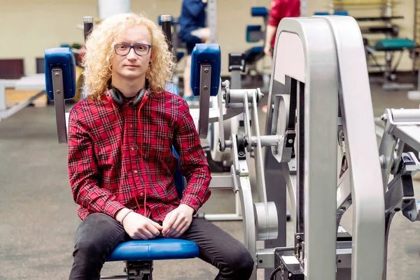 Curly blond guy with glasses and red headphones in the gym.