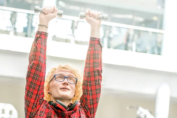 Loser in glasses lifting small dumbbells in the gym.