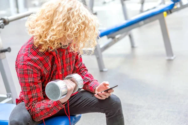 Curly blonde guy in a red shirt  holding in his hands dumbbell a