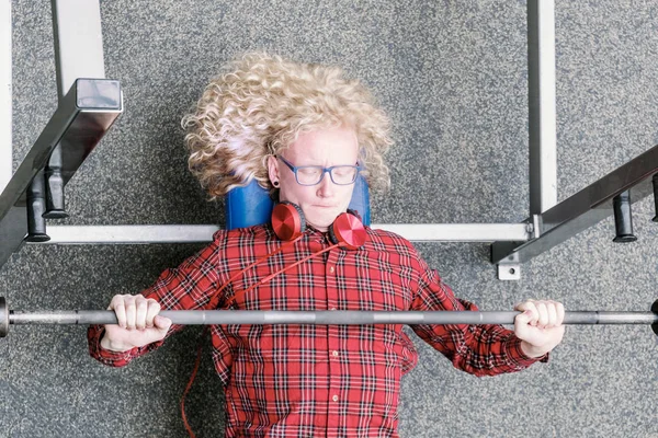 Cara fraco com cabelo louro encaracolado tensamente detém um barbell no gy — Fotografia de Stock