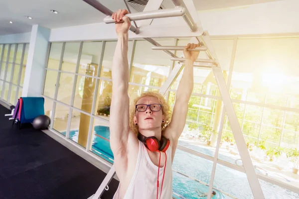 Fitnessstudio. Müder blonder Lockenkopf mit Brille, der an der Querlatte hängt. — Stockfoto