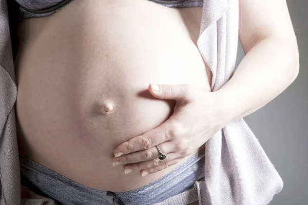 Pancia di una donna incinta con una mano su di esso da vicino . — Foto Stock