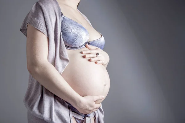 Donna incinta su sfondo grigio in studio tenendosi per mano — Foto Stock