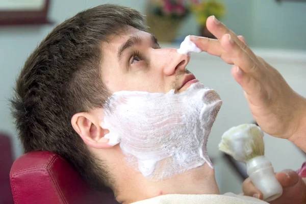 Молодой человек в парикмахерской, бреется . — стоковое фото