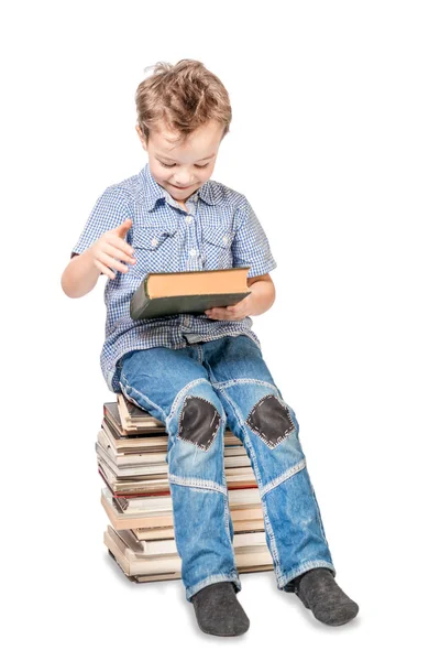 Lindo chico sonriente con un libro está sentado en un montón de libros. Isol — Foto de Stock