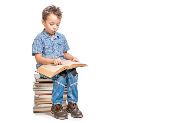 Un chico lindo está sentado en una pila de libros y leyendo un libro sobre — Foto de Stock