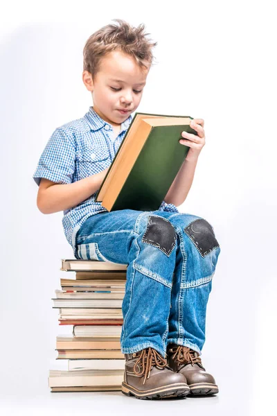 Carino ragazzo seduto su un mucchio di libri e la lettura di un libro su un whit — Foto Stock