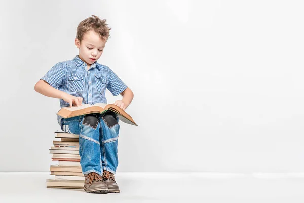 Lindo chico sentado en una pila de libros y hojeando un libro — Foto de Stock