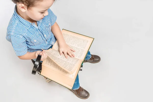 Lindo chico con una lupa leyendo un libro, vista superior . — Foto de Stock