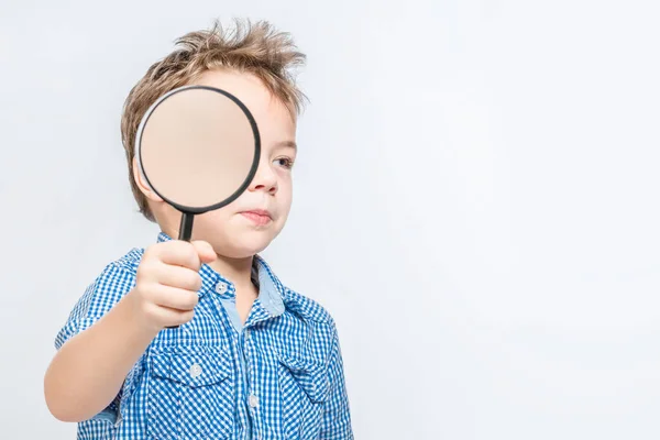 Carino ragazzo con una lente di ingrandimento tra le mani su un dorso bianco — Foto Stock