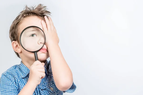 Carino ragazzo guarda in una lente di ingrandimento con un occhio, l'altro c — Foto Stock