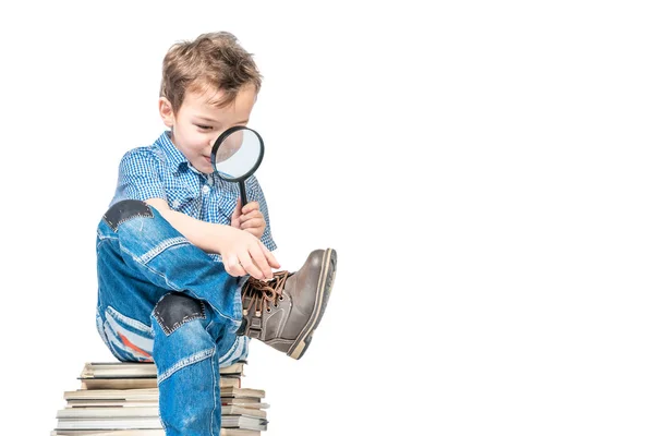 Rapaz bonito com uma lupa sentado em uma pilha de livros em um — Fotografia de Stock