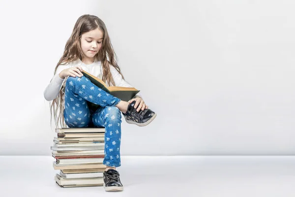 Linda chica sentada en una pila de libros y leyendo un libro en un wh — Foto de Stock