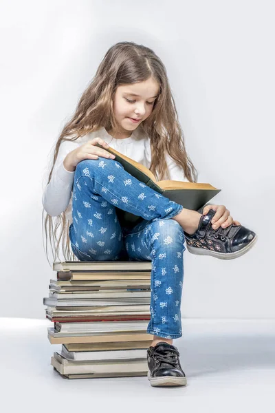Linda chica sentada en una pila de libros y leyendo un libro en un wh — Foto de Stock