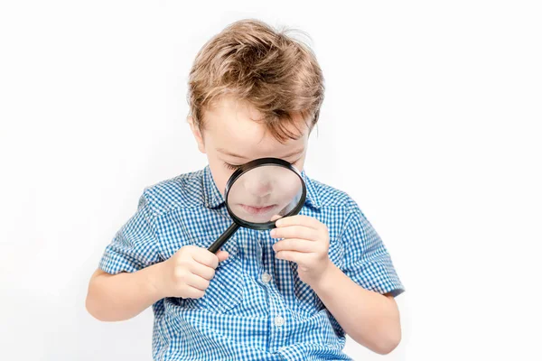 Carino serio ragazzo guardando attraverso un lente di ingrandimento su un bianco b — Foto Stock