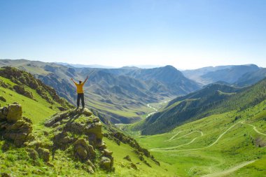 Elleri dağlardan birinin tepesinde olan bir adam..