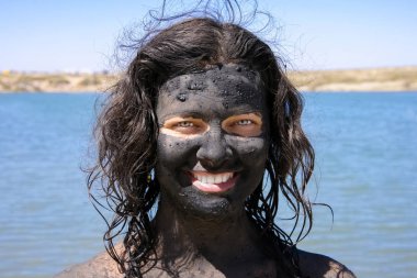 Yüzünde şifa çamuru ile gülümseyen kadın.