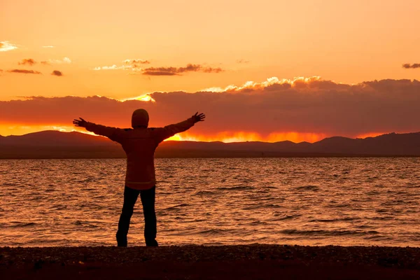 Silhouette with arms outstretched towards sunset over the lake.