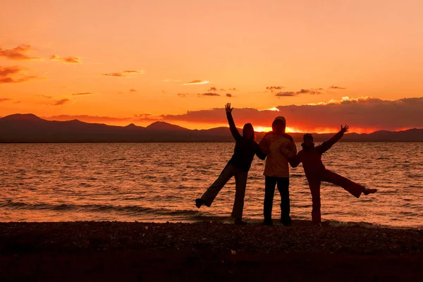 Three silhouettes at sunset by the lake. — Stock Photo, Image